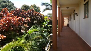 A covered corridor with a tiled floor, surrounded by lush greenery and a variety of plants. - Zawadi Hotel (Adjumani)