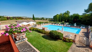 Ein Pool mit Liegestühlen und Sonnenschirmen, umgeben von einem gepflegten Rasen und Garten.