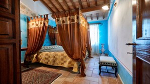 Ein Schlafzimmer mit einem Himmelbett, einer Bank, einem kleinen Tisch und einer Ziervase.