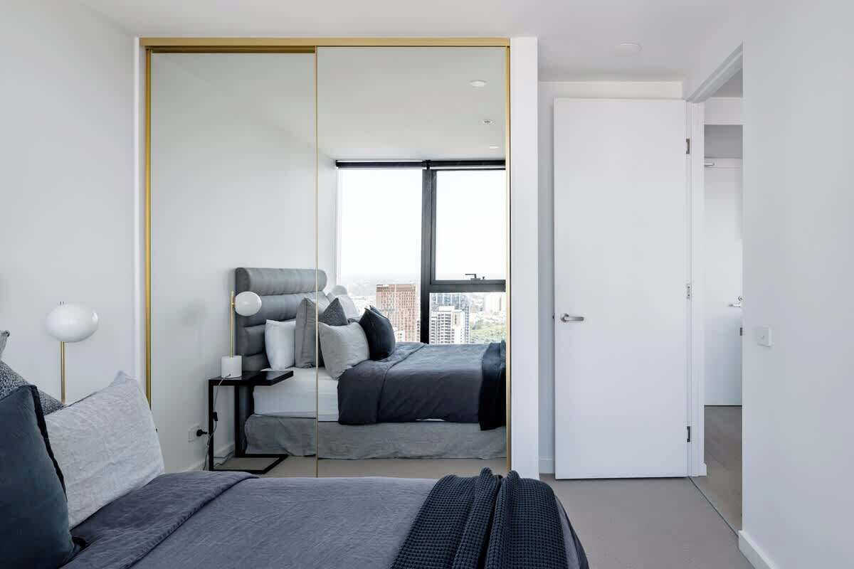 A modern bedroom with a bed, bedside table, lamp, and a large mirror.