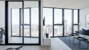 A modern living room with large floor-to-ceiling windows, a flat-screen TV, a sofa, and a coffee table.