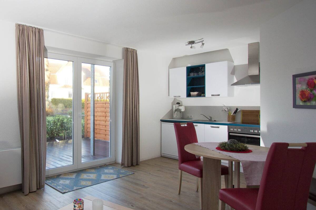 Cocina compacta con comedor, puerta corrediza de vidrio a un patio y una pequeña mesa con sillas.