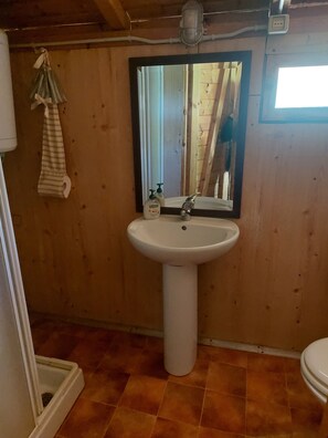 Un baño con un lavabo blanco sobre pedestal, un espejo con marco negro y piso de madera.