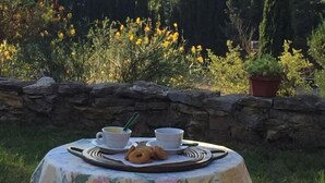 A table with a floral tablecloth, two cups, a plate with pastries, and a view of a countryside landscape with trees and hills. - Casale Sant'Elia (Capranica)