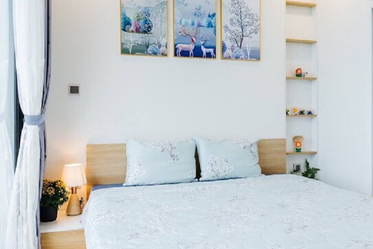 Een slaapkamer met een bed, twee kussens, een nachtkastje met een lamp, en drie ingelijste foto's aan de muur.