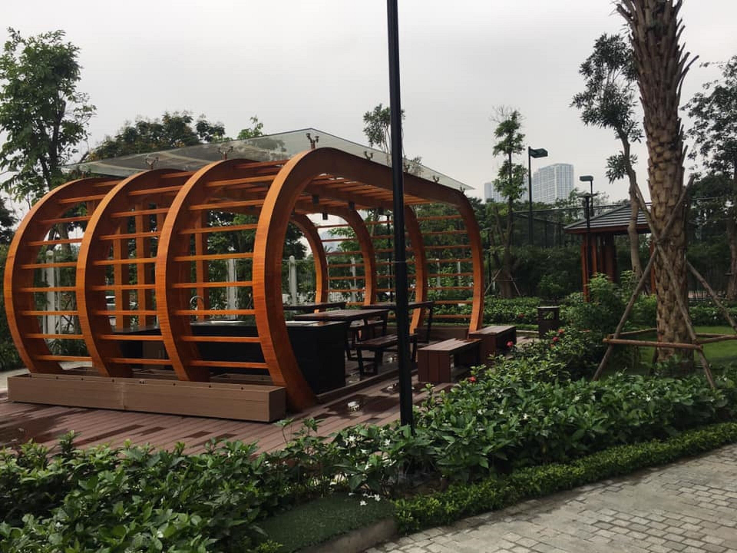 A wooden structure with a glass roof, surrounded by greenery and a paved walkway.