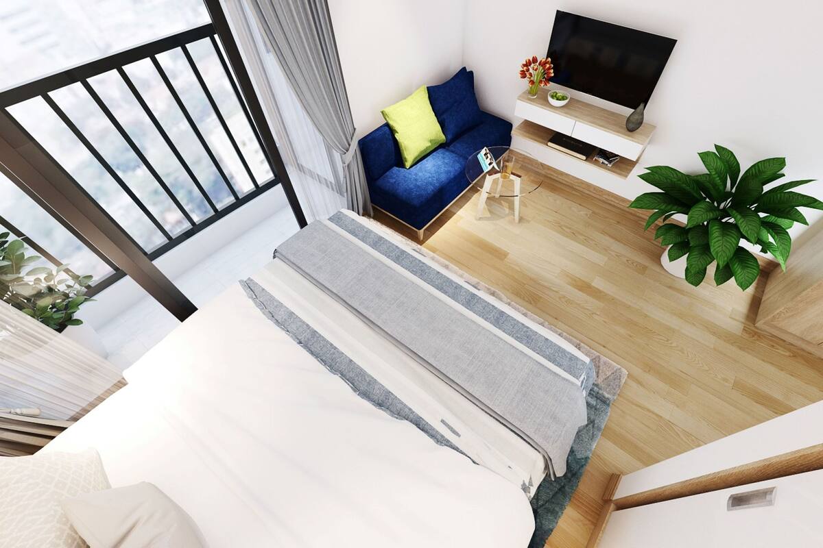 Een moderne hotelkamer met een groot raam, een bank met een blauw kussen, een flatscreen televisie, een klein tafeltje met een bloemenvaas, en een kamerplant.