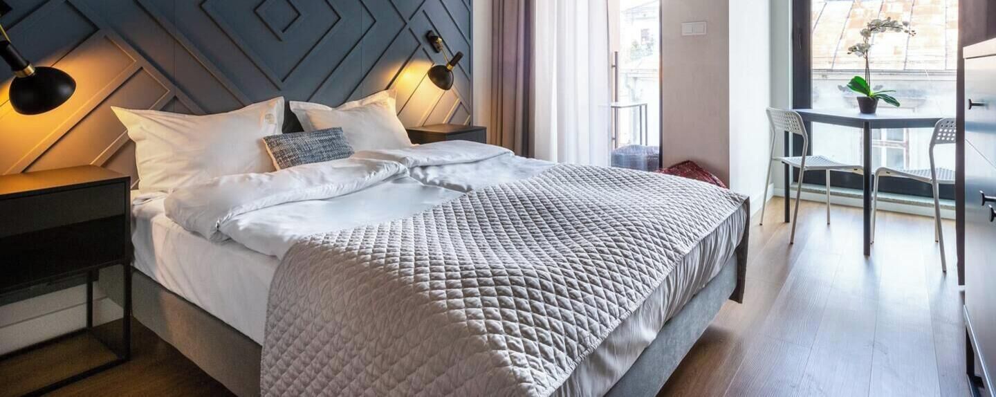 A neatly made bed with a quilted blanket, a bedside lamp, and a small table with chairs.