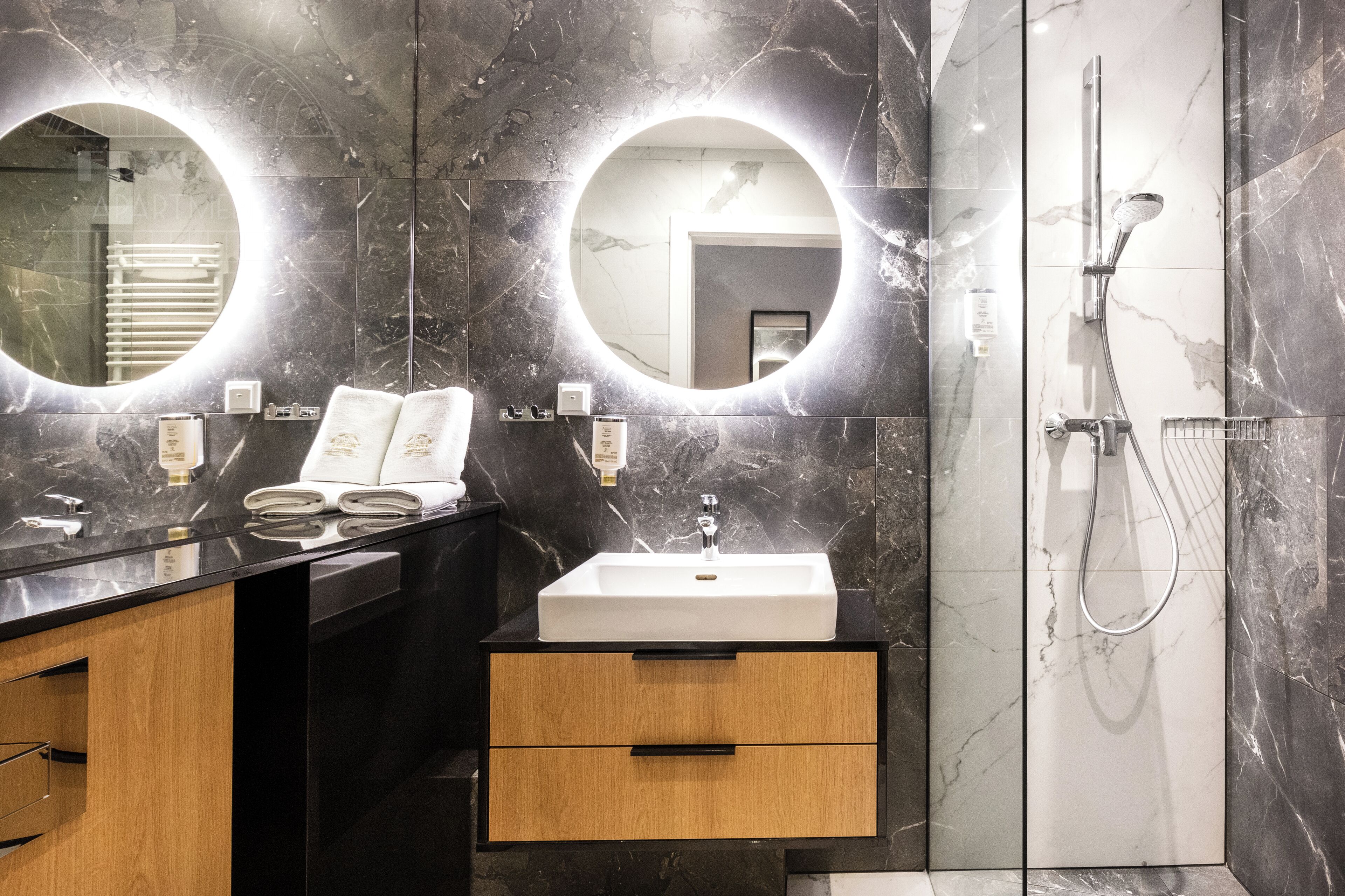 Un baño moderno con un lavamanos de mármol negro, dos cajones de madera y una ducha con cabezal de ducha manual.
