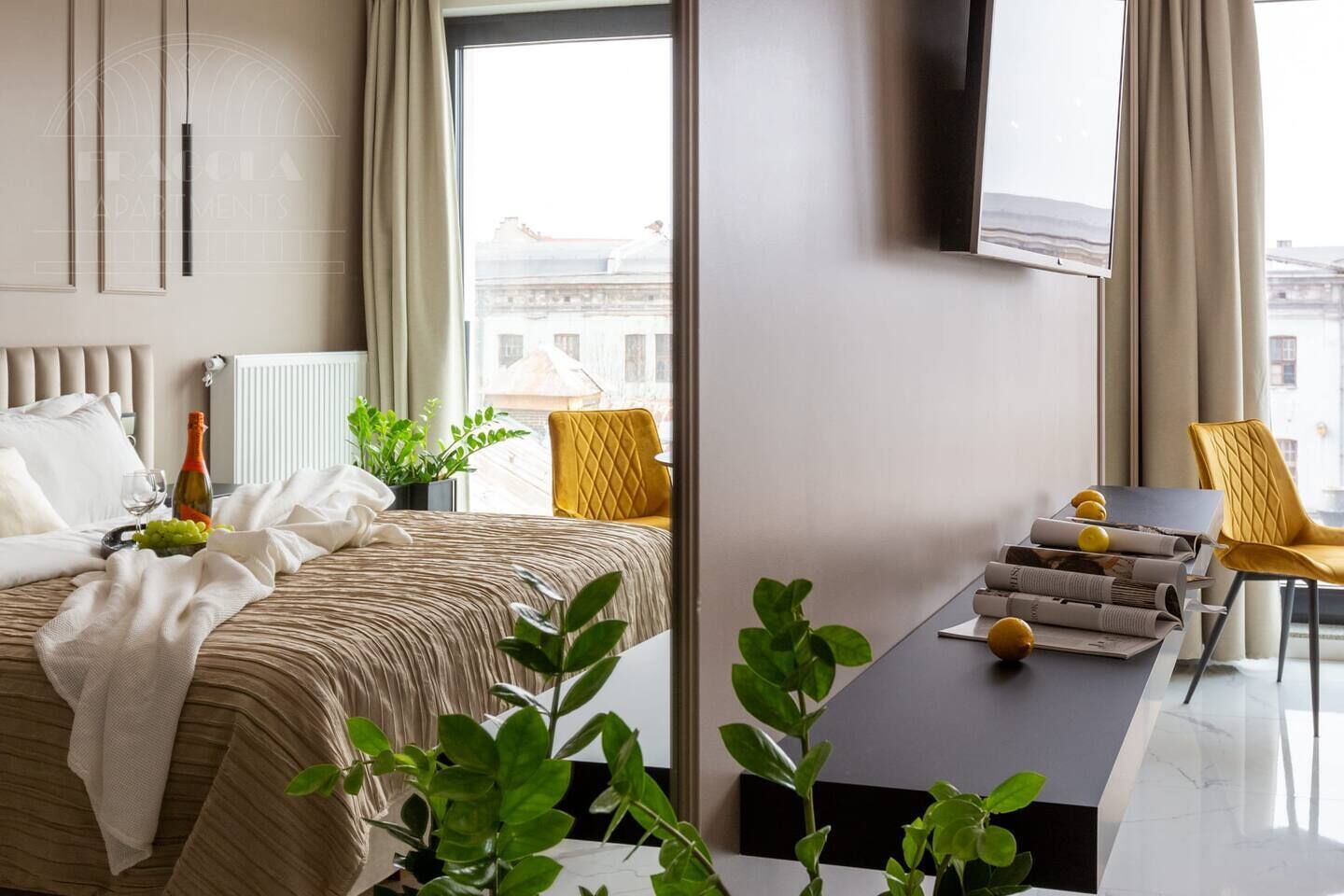 A hotel room with a bed, a table with newspapers, a plant, and a window with a view of buildings.