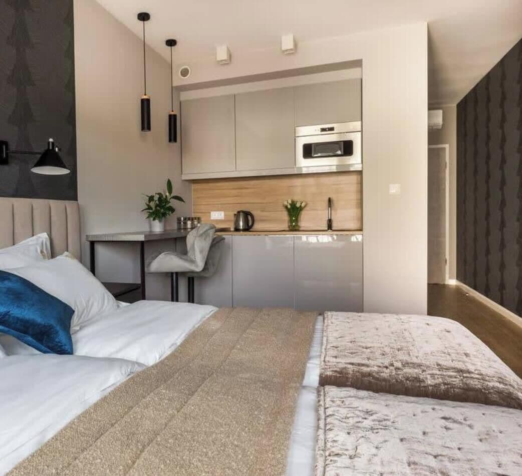 A modern bedroom with a bed, bedside tables, and a built-in kitchen area with a microwave.