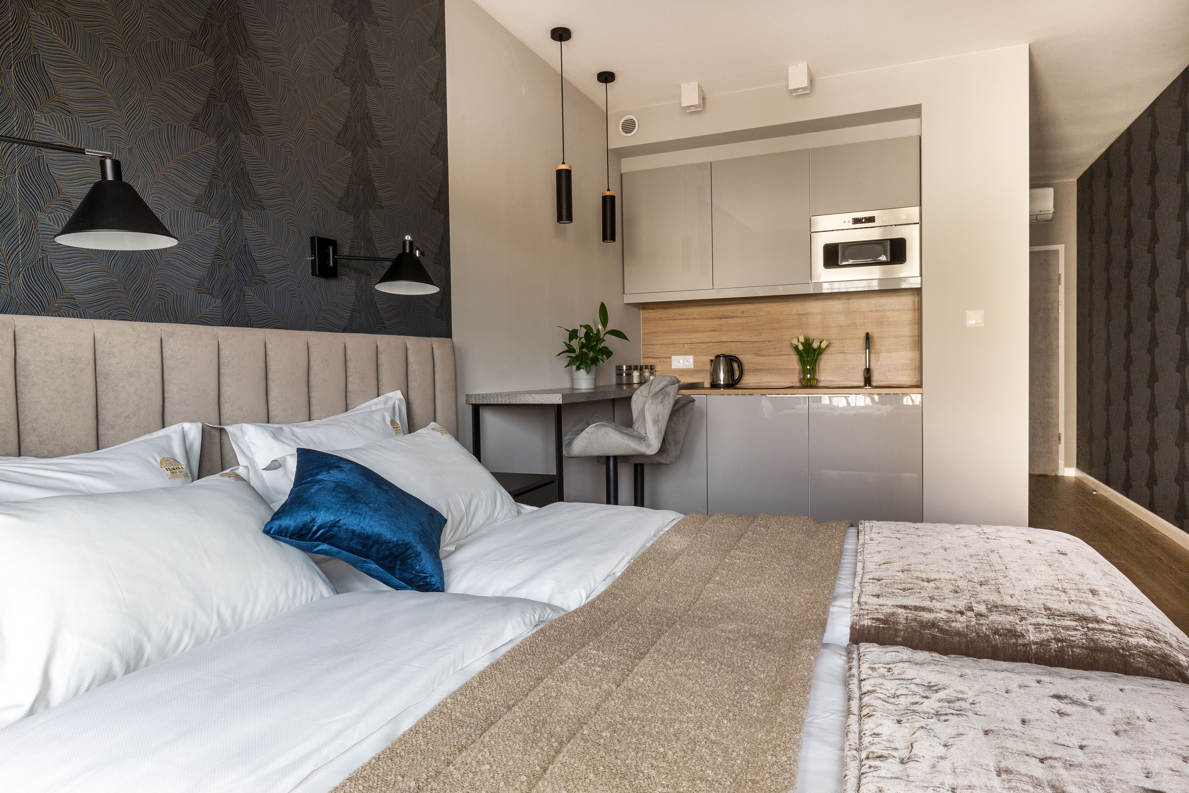 A modern bedroom with a bed, bedside tables, a desk, and a kitchenette.