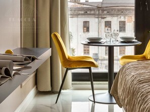 A modern hotel room with a bed, a dining table with chairs, a window with a view of old buildings, and a newspaper on the side table. - Rajska 3 by Fragola Apartments (Kraków)