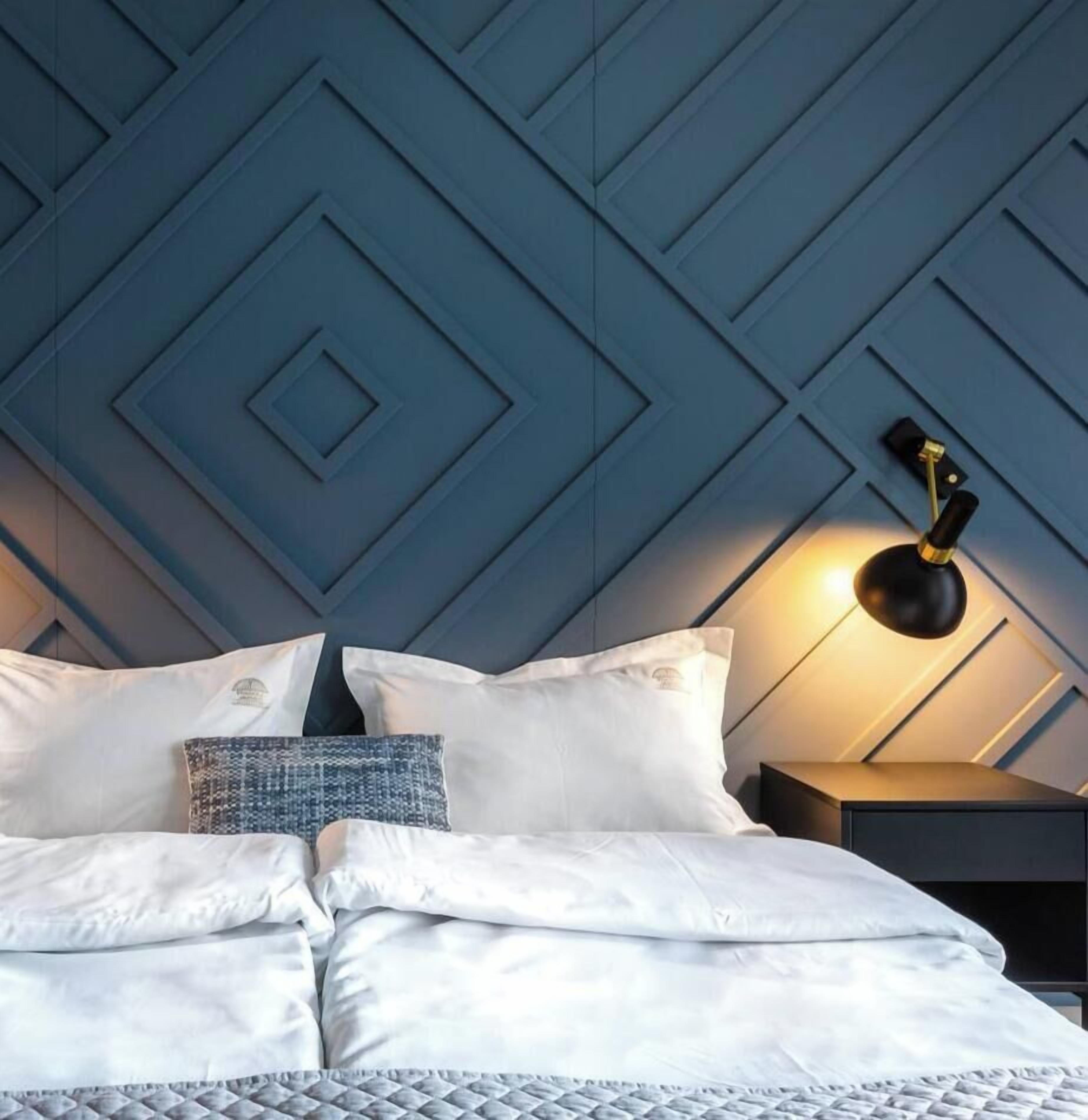 A bed with white bedding, a patterned pillow, and a wall with a geometric design.
