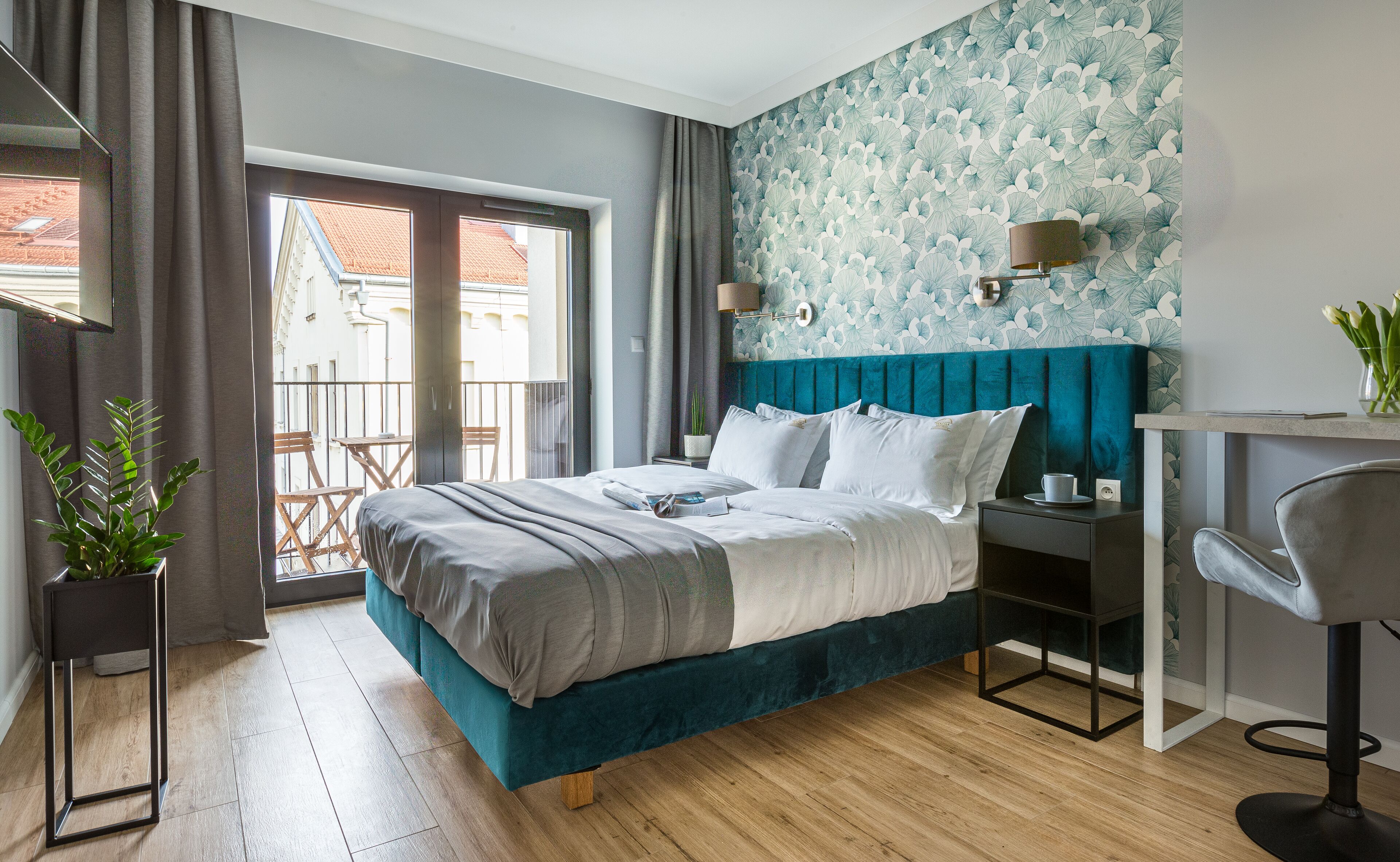 Ein modernes Schlafzimmer mit einem moosgrünen Bettenvorhang, Holzboden, einem Balkon mit Blick auf Gebäude und einem Schreibtisch mit Stuhl.
