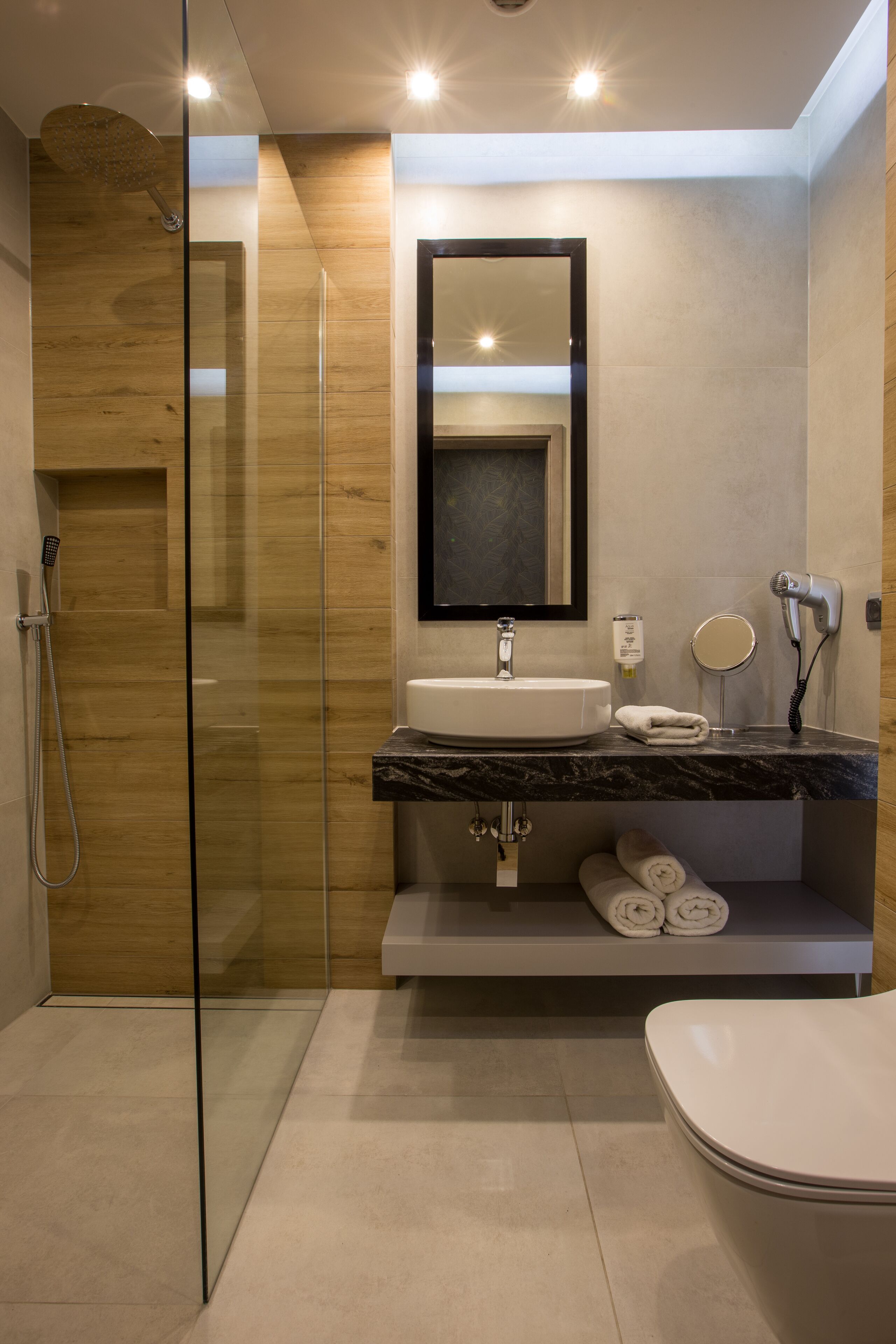 Un baño moderno con ducha envuelta en vidrio, lavamanos de mármol, espejo integrado y un inodoro.