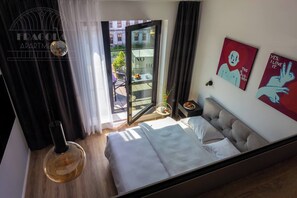 A modern bedroom with a bed, a glass door to a balcony, and a view of buildings. - Rajska 3 by Fragola Apartments (Kraków)