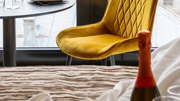 Ein Zimmer mit einem gelben Stuhl, einer Weinflasche, einer Schüssel mit Trauben und einem Tisch mit Gläsern und einem Teller.