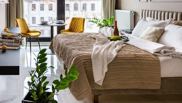 Ein modernes Schlafzimmer mit einem großen Bett, einem Esstisch und Blick auf Gebäude.