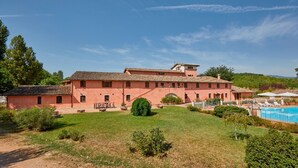 Un grand bâtiment à deux étages, doté d’un toit en tuiles, entouré d’une pelouse bien entretenue et d’une piscine.