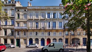Eine Reihe klassischer europäischer Gebäude mit einheitlicher Architektur, mit zahlreichen Fenstern und Türen, vor denen ein kleiner, weißer Van geparkt ist.