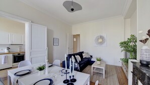 Eine moderne Küche mit weißen Schränken, ein Essbereich mit einem weißen Tisch, gedeckt für vier Personen, und ein dunkel gefärbtes Sofa im Wohnbereich.