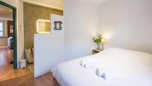 A hotel room with a large bed, a bedside table with a lamp, a small plant, and a wall-mounted mirror. - LE ROSA BONHEUR - One Bedroom Apartment, Sleeps 4 (Toulouse)