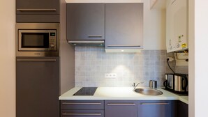 A modern kitchen with grey cabinets, a stainless steel microwave, a sink, and a kettle.