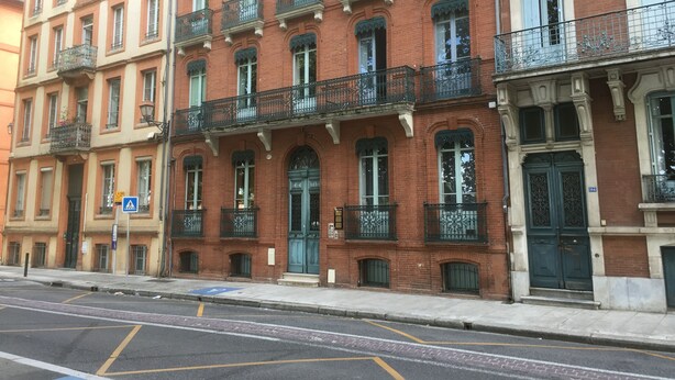 A row of red brick buildings with green balconies and white trim.