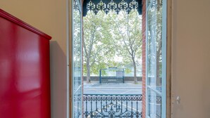 A view through a glass door with a metal railing, leading to an outdoor area with trees and a bench.