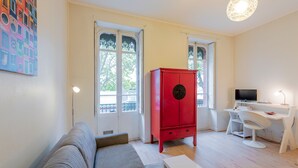 A modern living room with a grey sofa, a red cabinet, a white desk, and a TV.