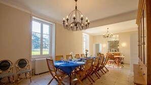 A dining room with a large table set for six, wooden chairs, a chandelier, and a view of the outdoors through a window.