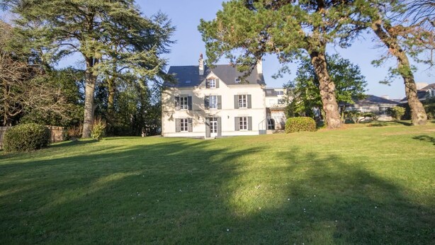 A two-story house with a well-maintained lawn and large trees in the foreground.