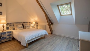 A bedroom with a sloped ceiling, a bed with white bedding, a nightstand with a lamp, and a window with a view of trees.
