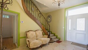A staircase with a wooden handrail and a chandelier, a beige armchair, and a white door with a window.