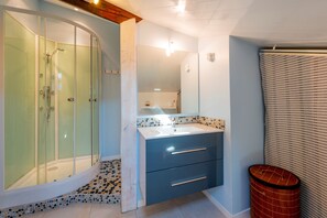 A modern bathroom with a glass-enclosed shower, a vanity with a mirror, and a tiled floor.