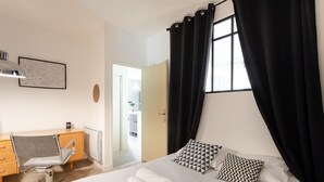 Una camera d'albergo con un letto, una scrivania, una sedia e una finestra con tende.
