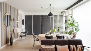 Un'area pranzo moderna con un tavolo rotondo, sedie nere e una lampada a sospensione nera. In primo piano, un divano con cuscini decorati.