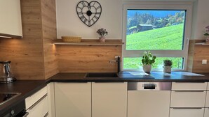 Une cuisine moderne dotée d’un lave-vaisselle encastré, d’un pare-feu en bois et d’une grande fenêtre offrant une vue sur un paysage verdoyant.
