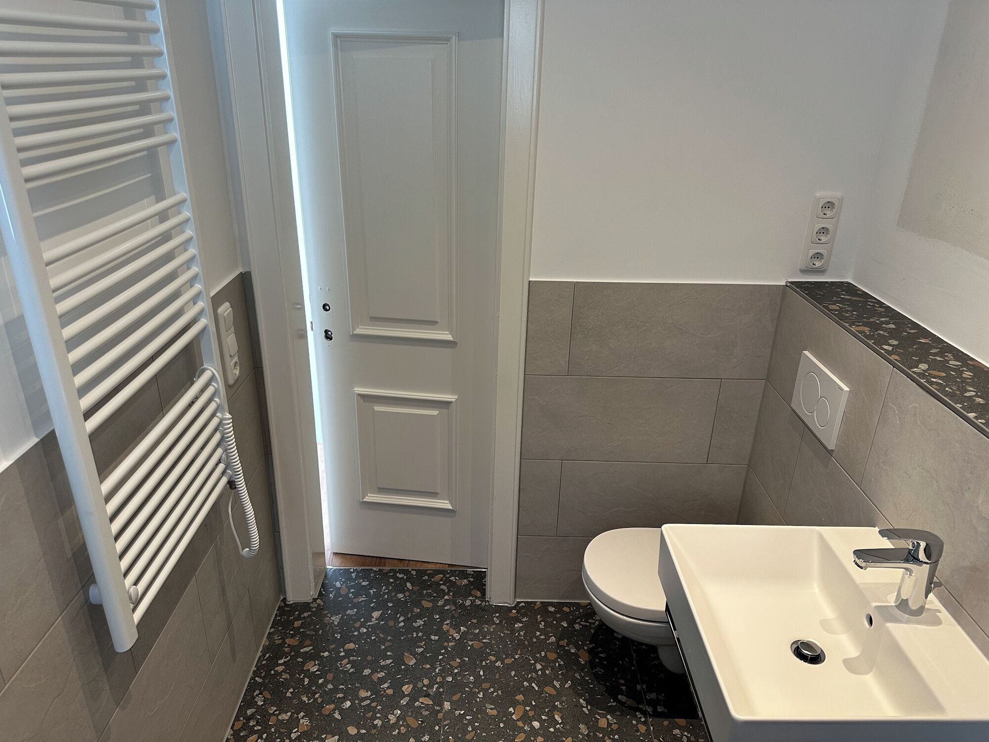 A compact bathroom with a toilet, sink, and radiator.