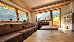 Un salon moderne avec un canapé d’angle en cuir marron, une table basse en bois et de grandes fenêtres offrant une vue sur les montagnes.