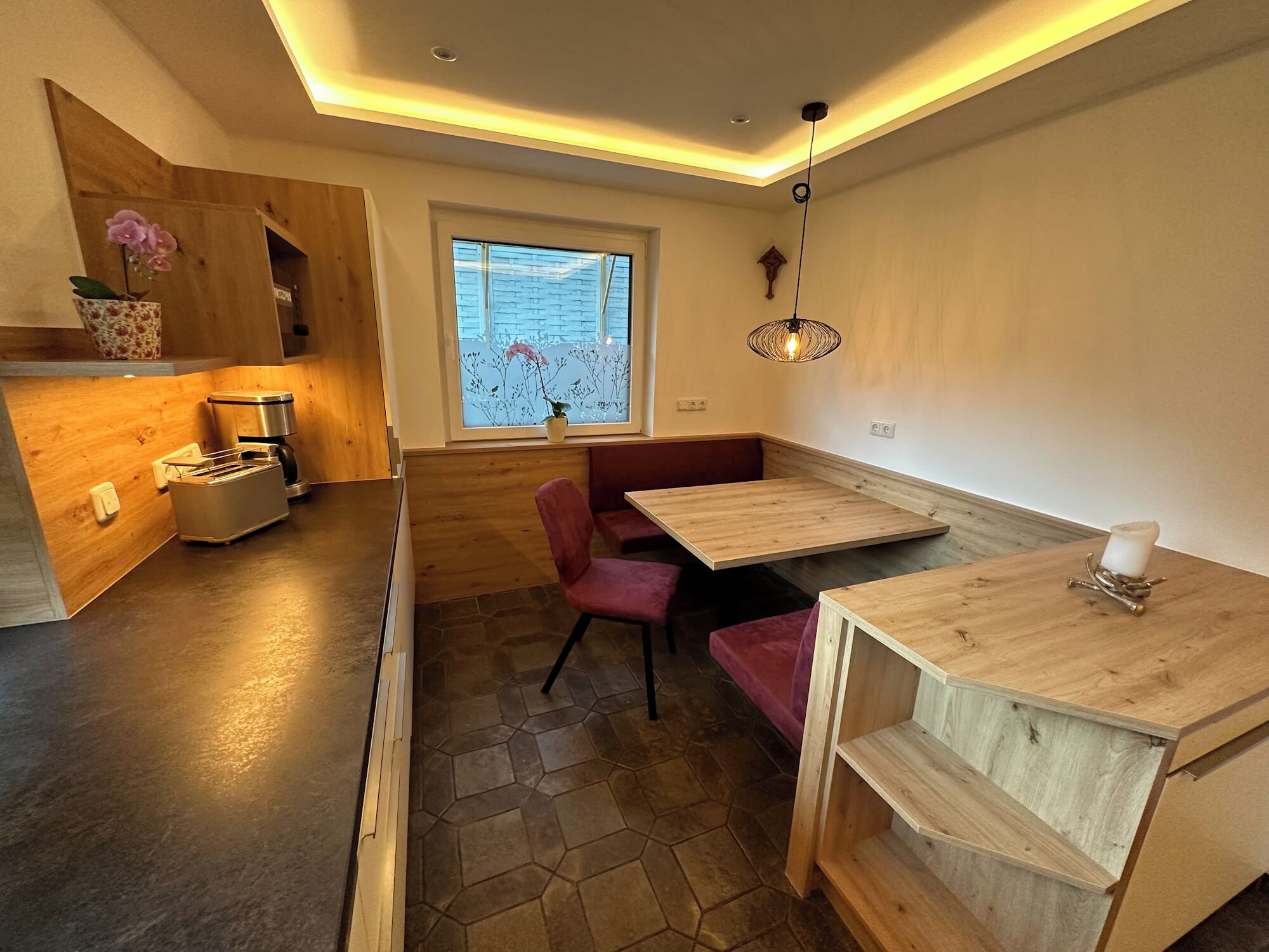 A modern kitchen with wooden cabinets, a built-in toaster, and a window with a view of the outside.