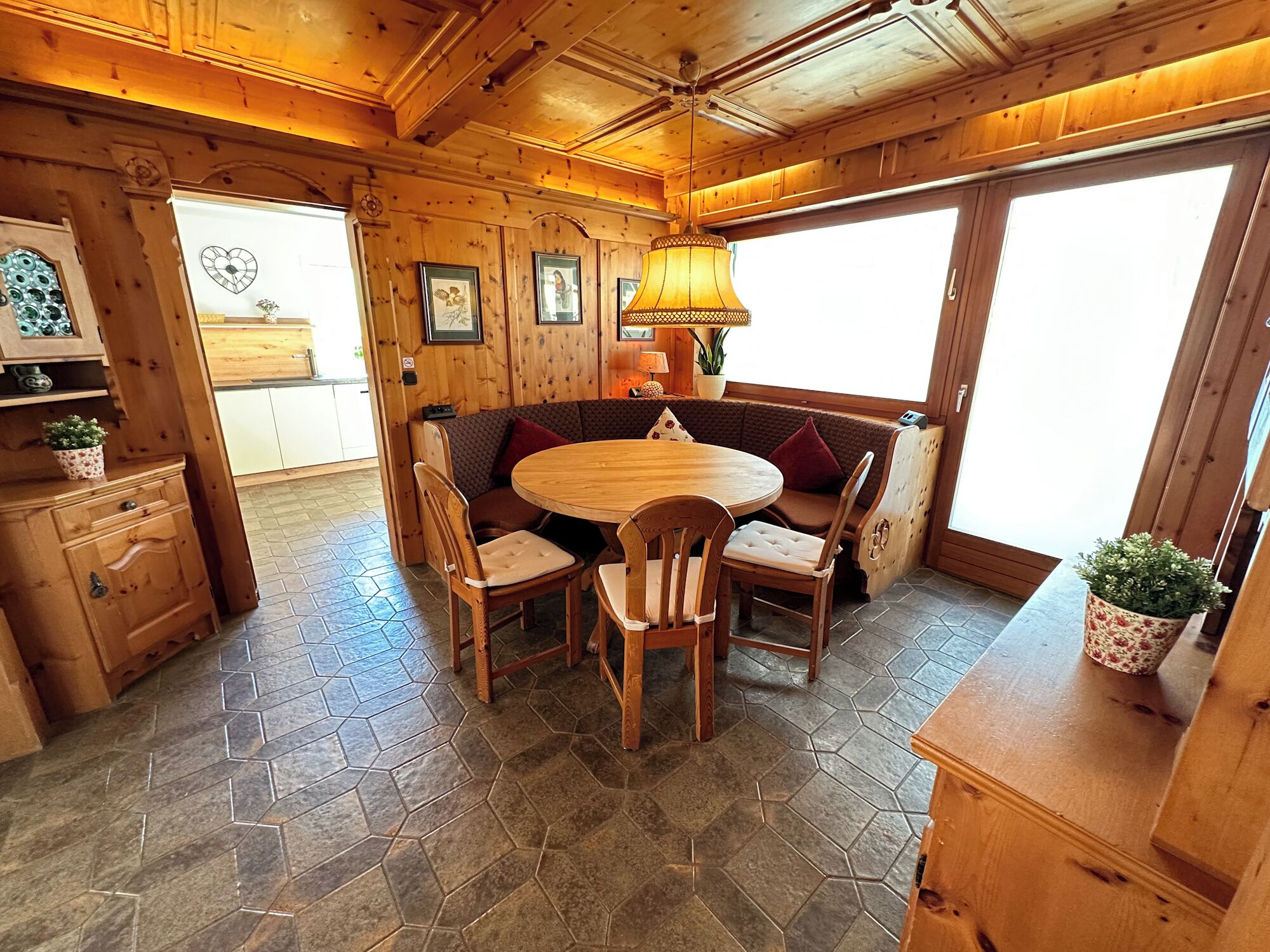 Un intérieur en bois avec une table ronde et des chaises, un banc et une grande fenêtre.