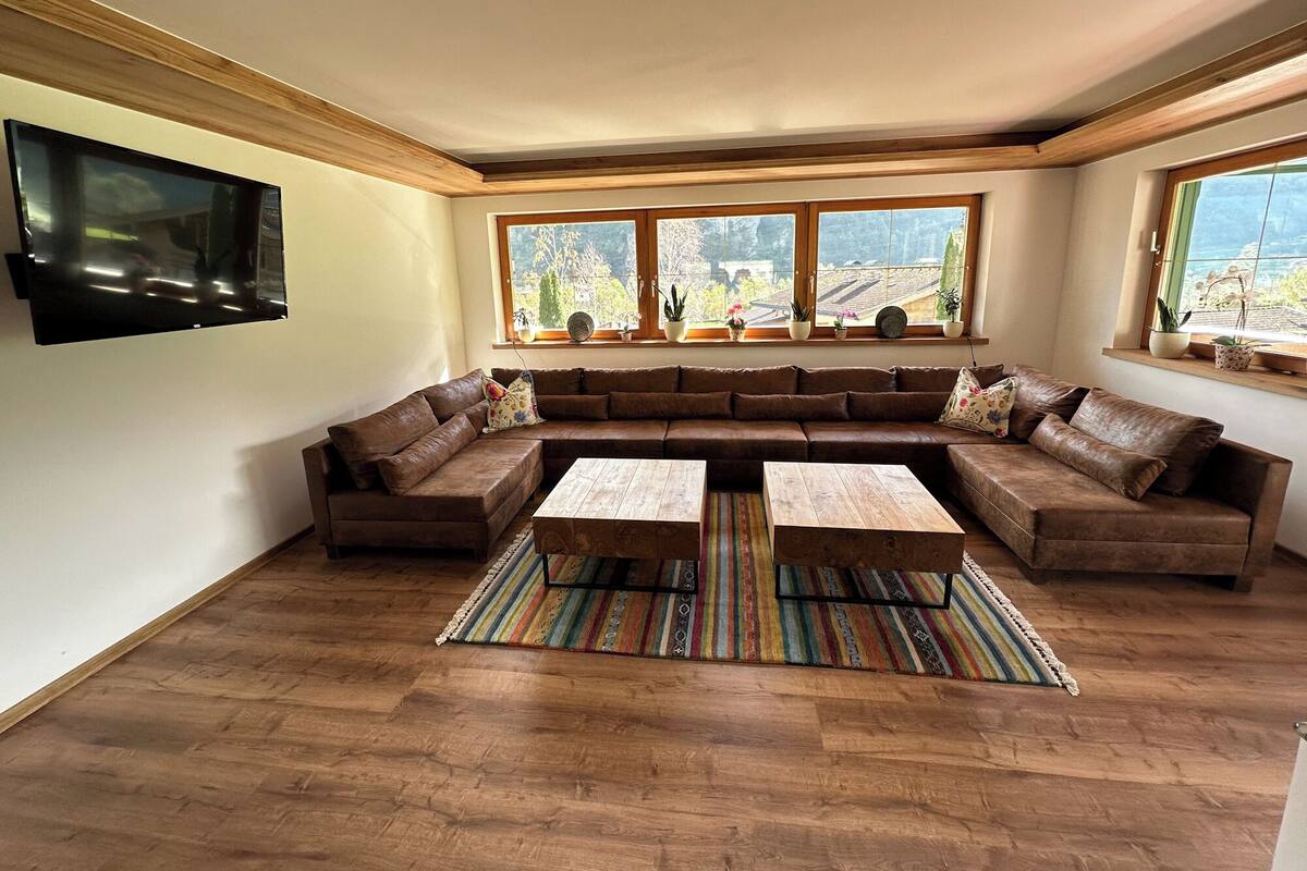 Un salon spacieux avec un grand canapé d’angle, deux tables basses en bois et un tapis rayé aux couleurs vives.