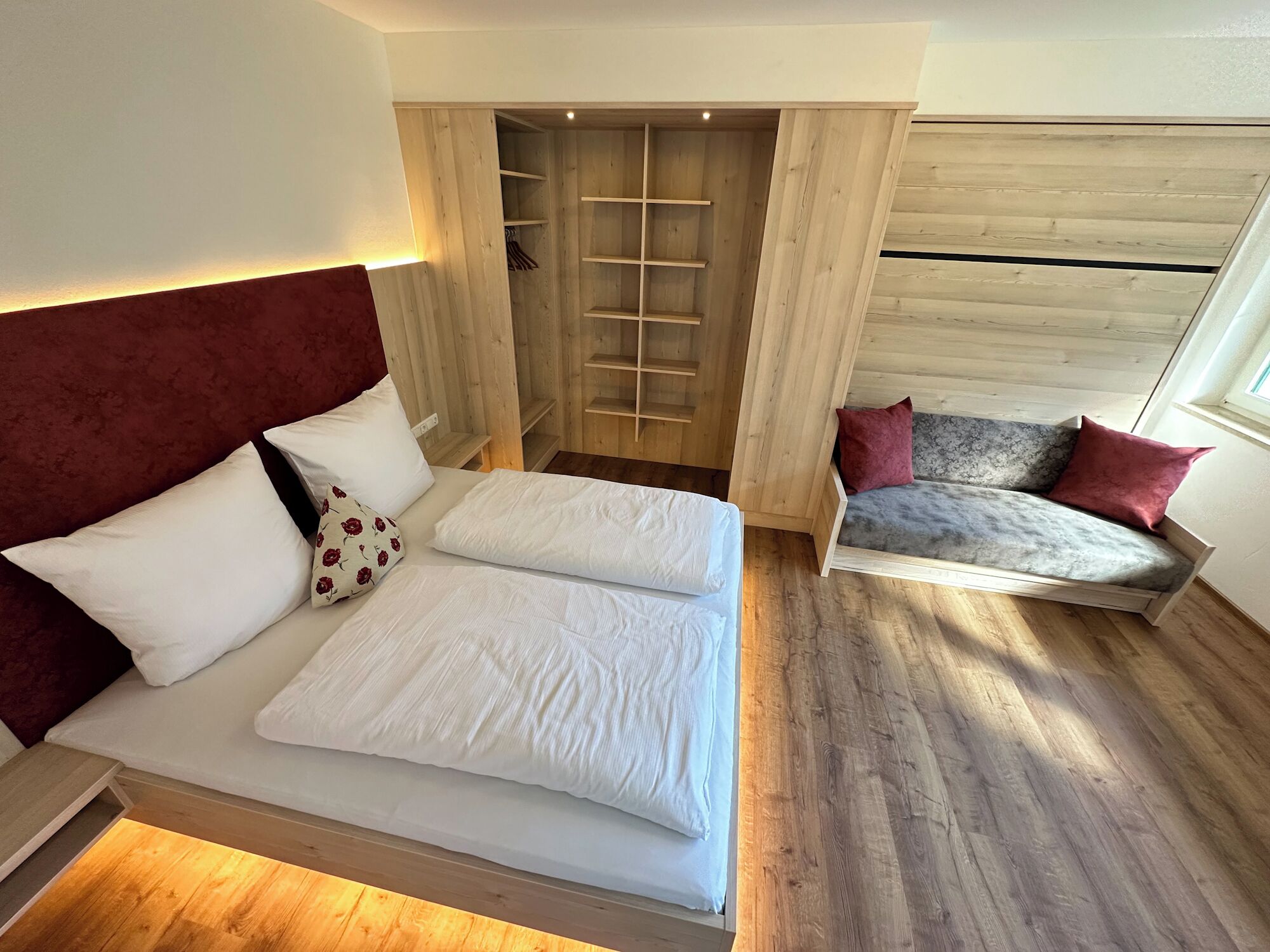 A bedroom with a bed, a sofa, a wooden wardrobe, and a window.