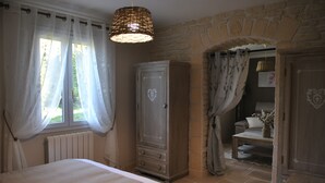 Un dormitorio con cama, armario, ventana con cortinas traslúcidas y pared de piedra.