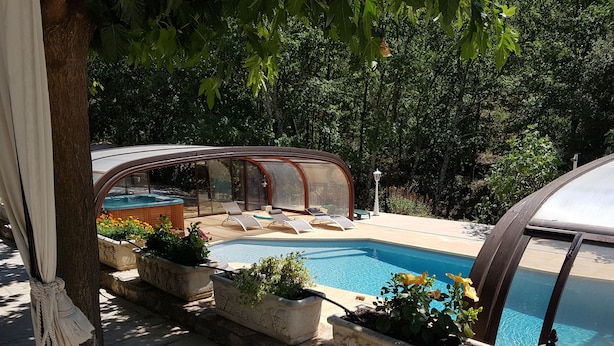 Zona de piscina con área de estar cubierta, plantas en macetas y un farol.