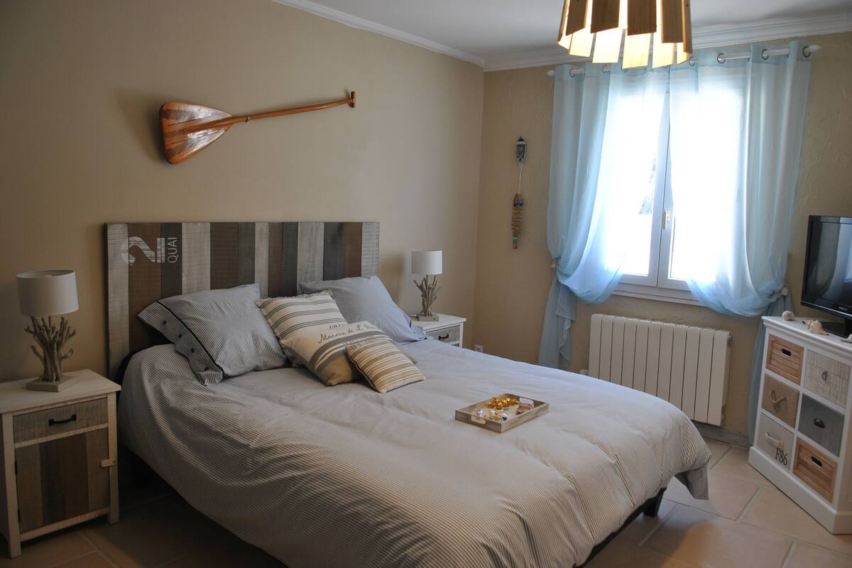 A neatly arranged bedroom with a large bed, bedside tables, a television, and a window with curtains.