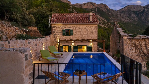 A stone building with a swimming pool, surrounded by mountains.