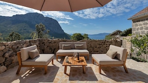 An outdoor seating area with a stone wall, a wooden table with a glass, a bottle, and a lantern.